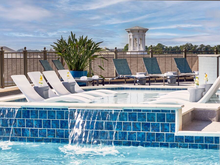 A rooftop pool with blue-tiled edges, lounge chairs, and a waterfall feature.