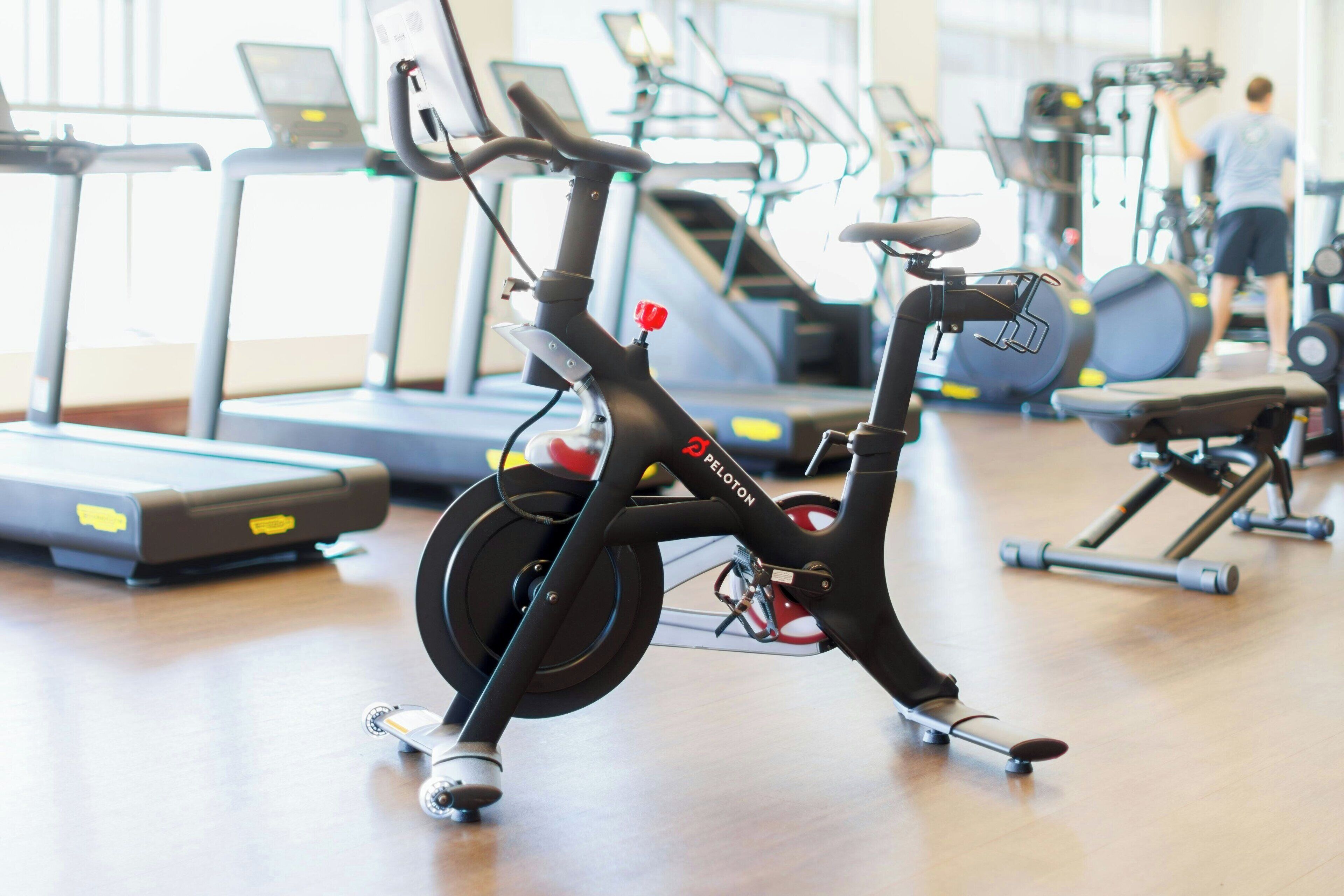 Una bicicleta estática en un gimnasio, con cintas de correr y elípticas al fondo.
