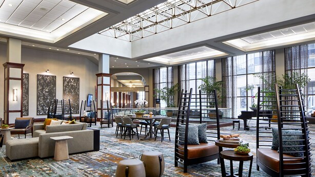 A spacious lobby with a high ceiling, large windows, and modern furniture.
