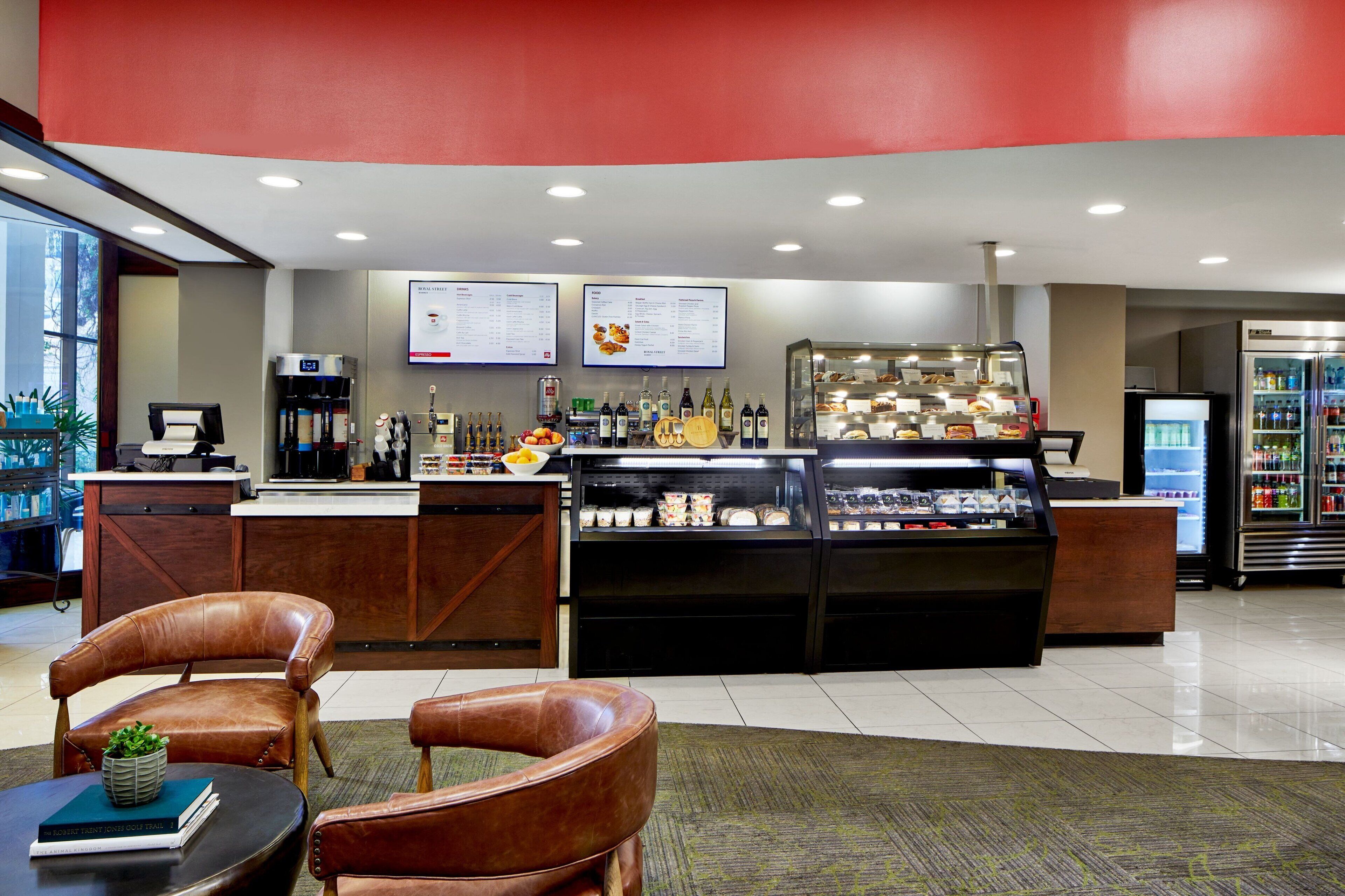 Um hall de hotel moderno com balcão de recepção, área de estar e vitrine com alimentos.