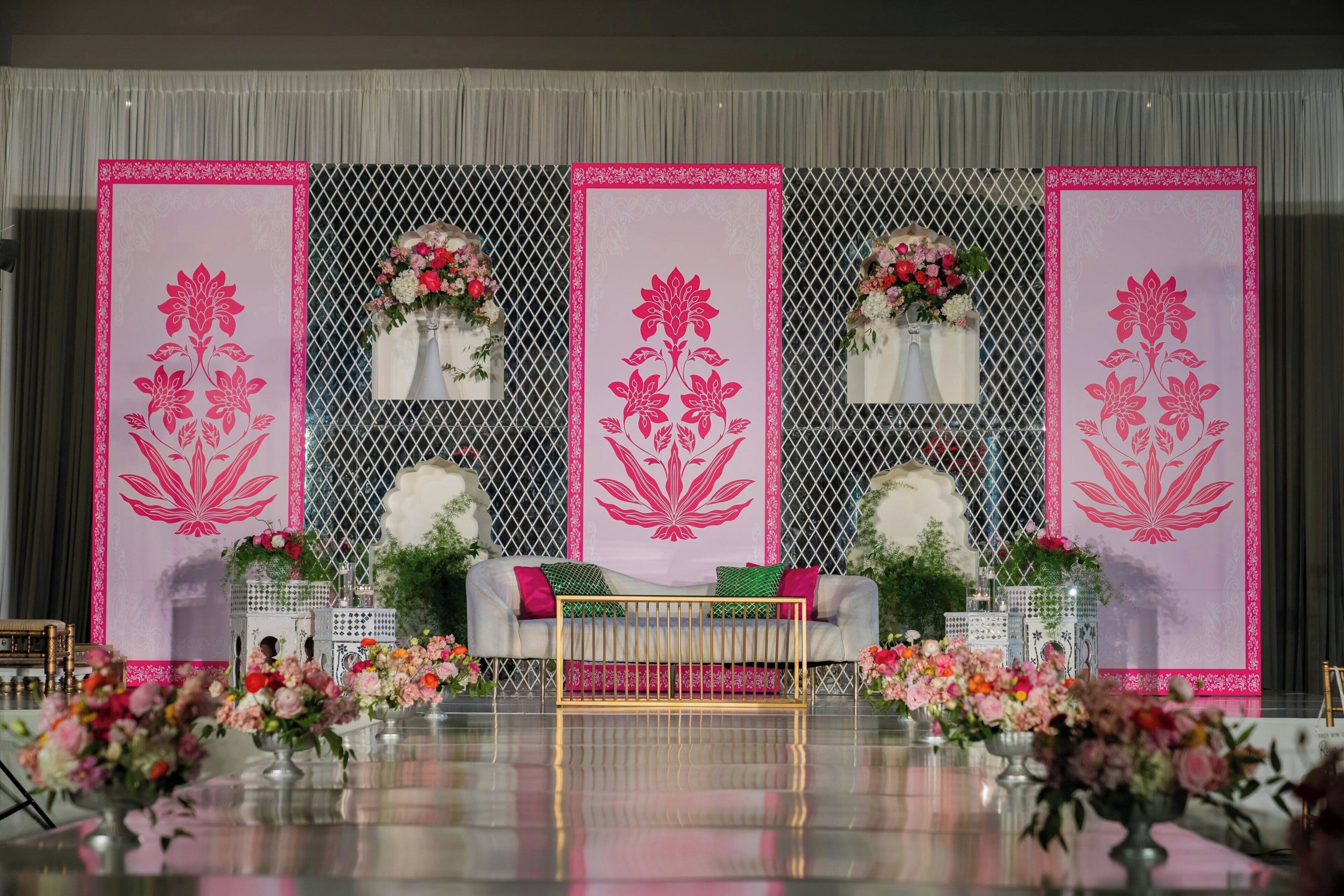 A stage with a white sofa, pink floral decorations, and a golden railing.