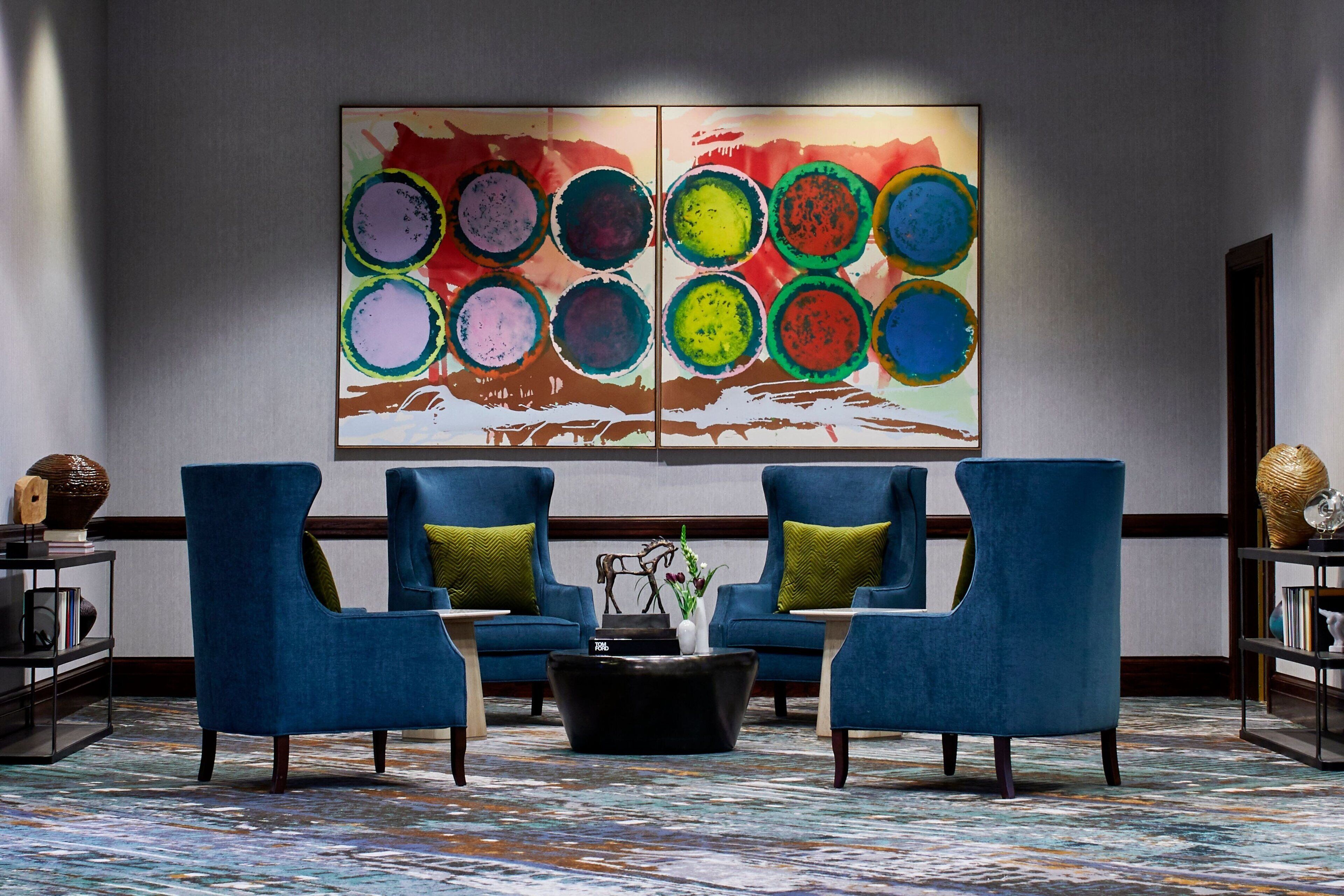 Un hall d’entrée avec deux fauteuils bleus, une table basse noire et un tableau abstrait aux couleurs vives accroché au mur.