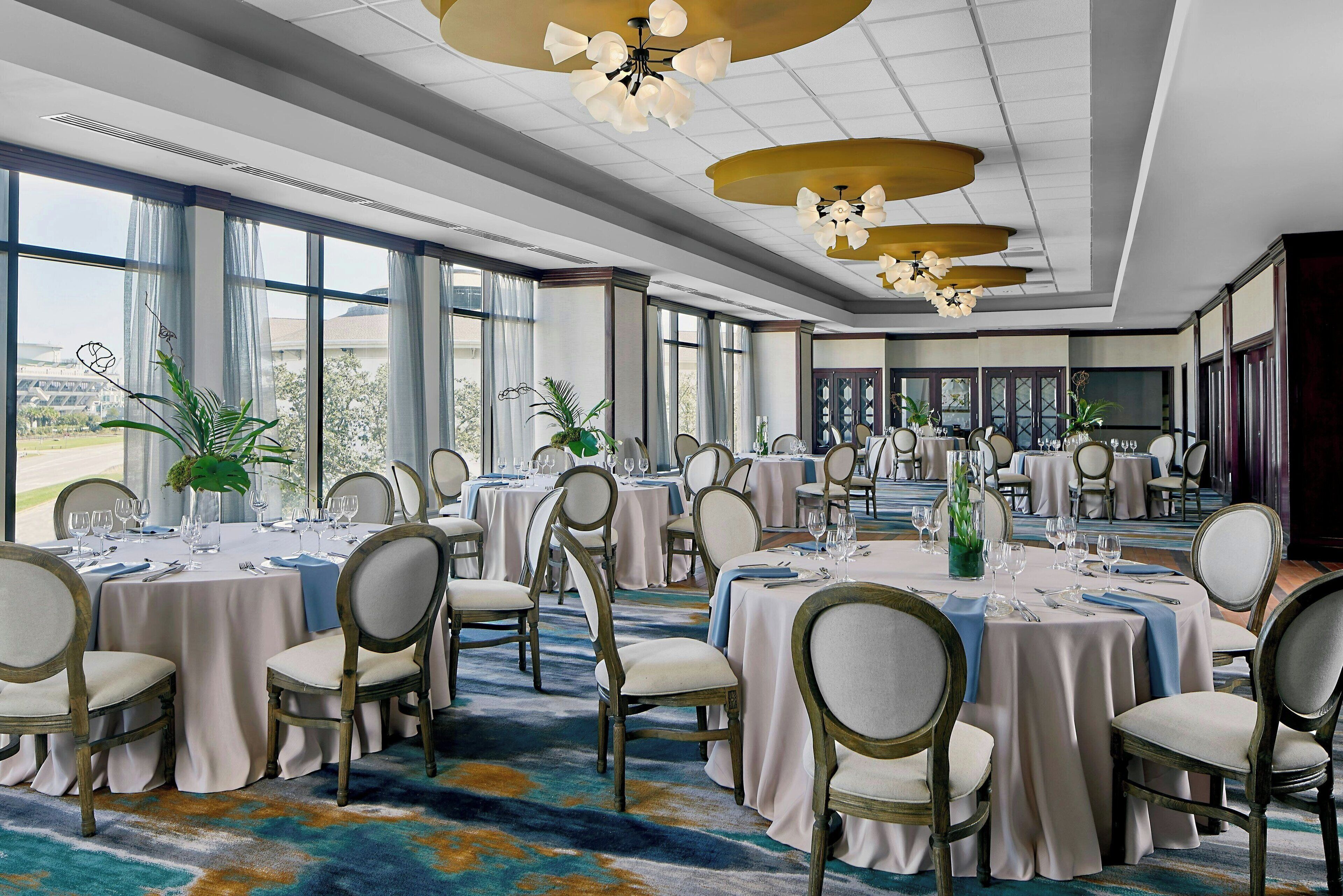 A banquet hall with round tables, chairs, and chandeliers.