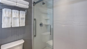A modern bathroom with a glass shower enclosure, a white toilet, and neatly folded towels on a rack. - Holiday Inn Mississauga Toronto West by IHG (Mississauga)