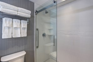 Un bagno moderno con cabina doccia in vetro, un water bianco e asciugamani ordinatamente piegati su un porta-asciugamani.