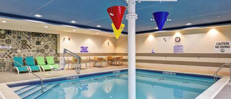 An indoor swimming pool with clear water, marked depth zones, and safety signs.