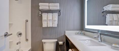 A modern bathroom with a bathtub, toilet, and sink. There are towels on a rack and a mirror above the sink.