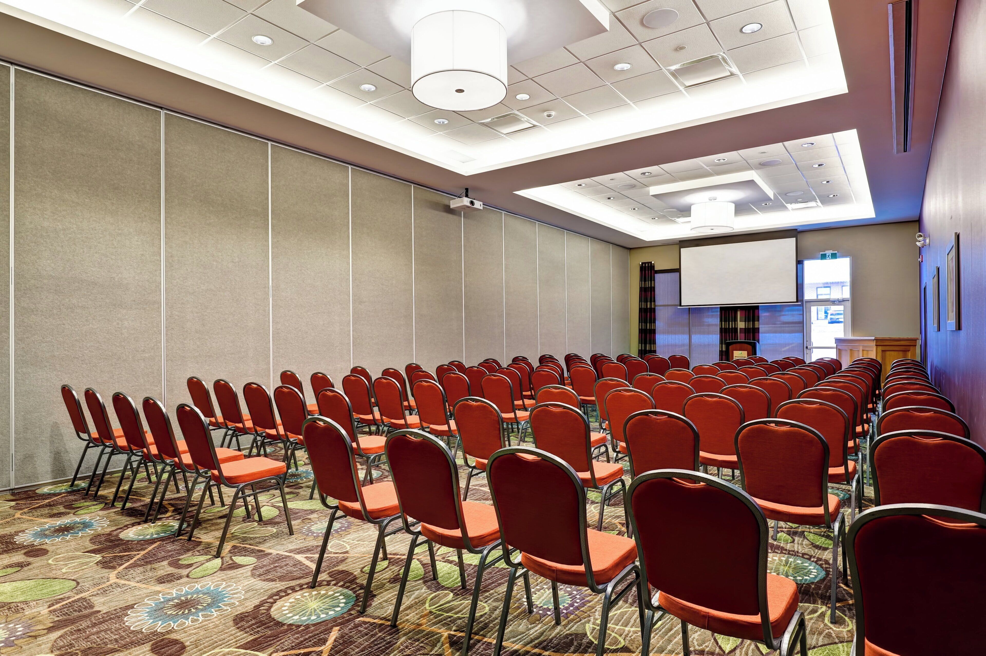 A conference room with rows of chairs, a projector screen, and a carpeted floor.