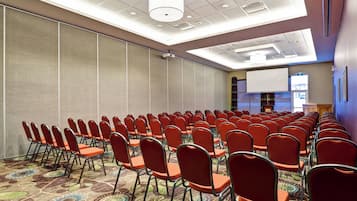 A conference room with rows of chairs, a projector screen, and a carpeted floor.