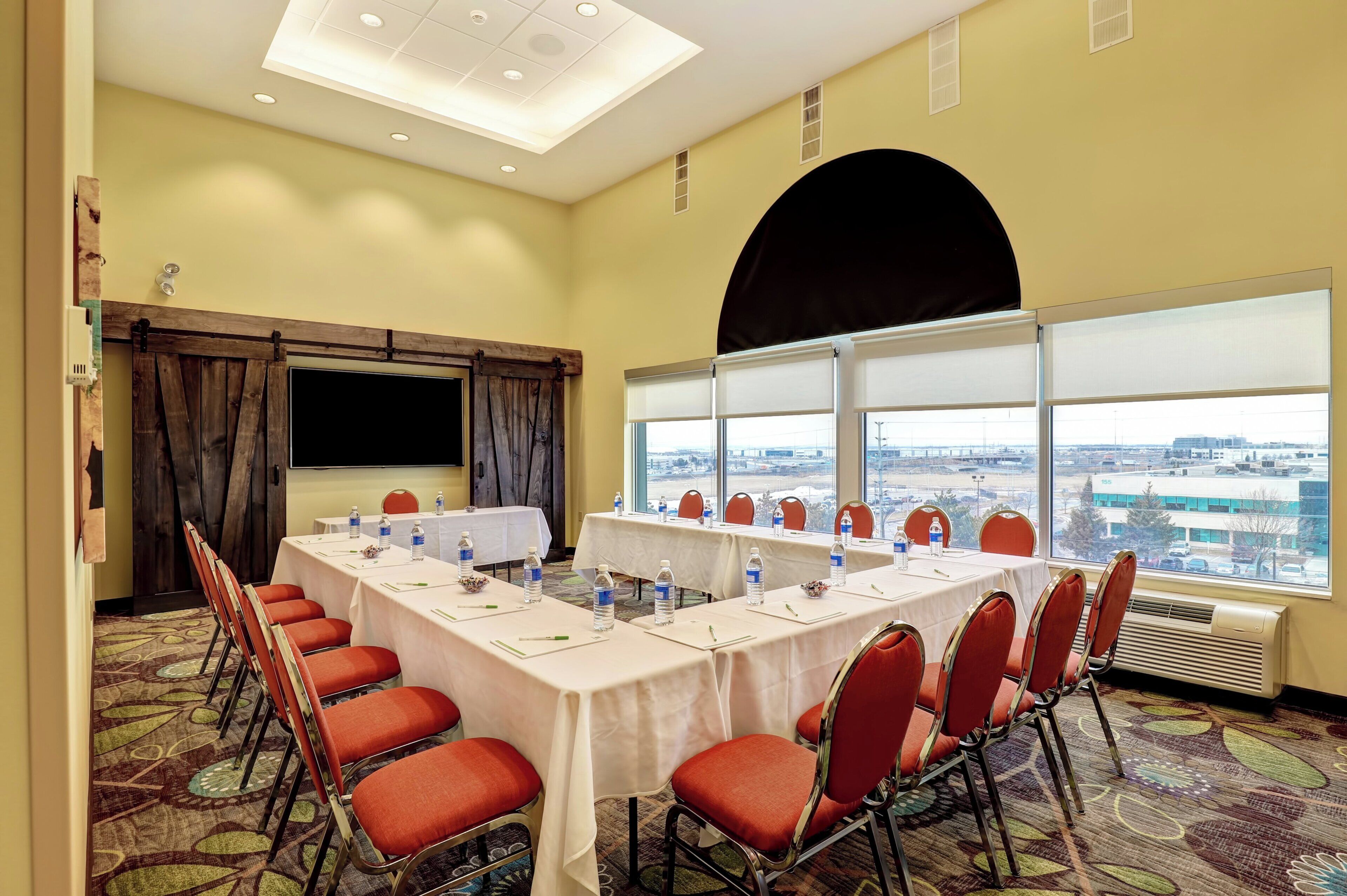 A conference room with a long table, red chairs, and a large window with a city view.