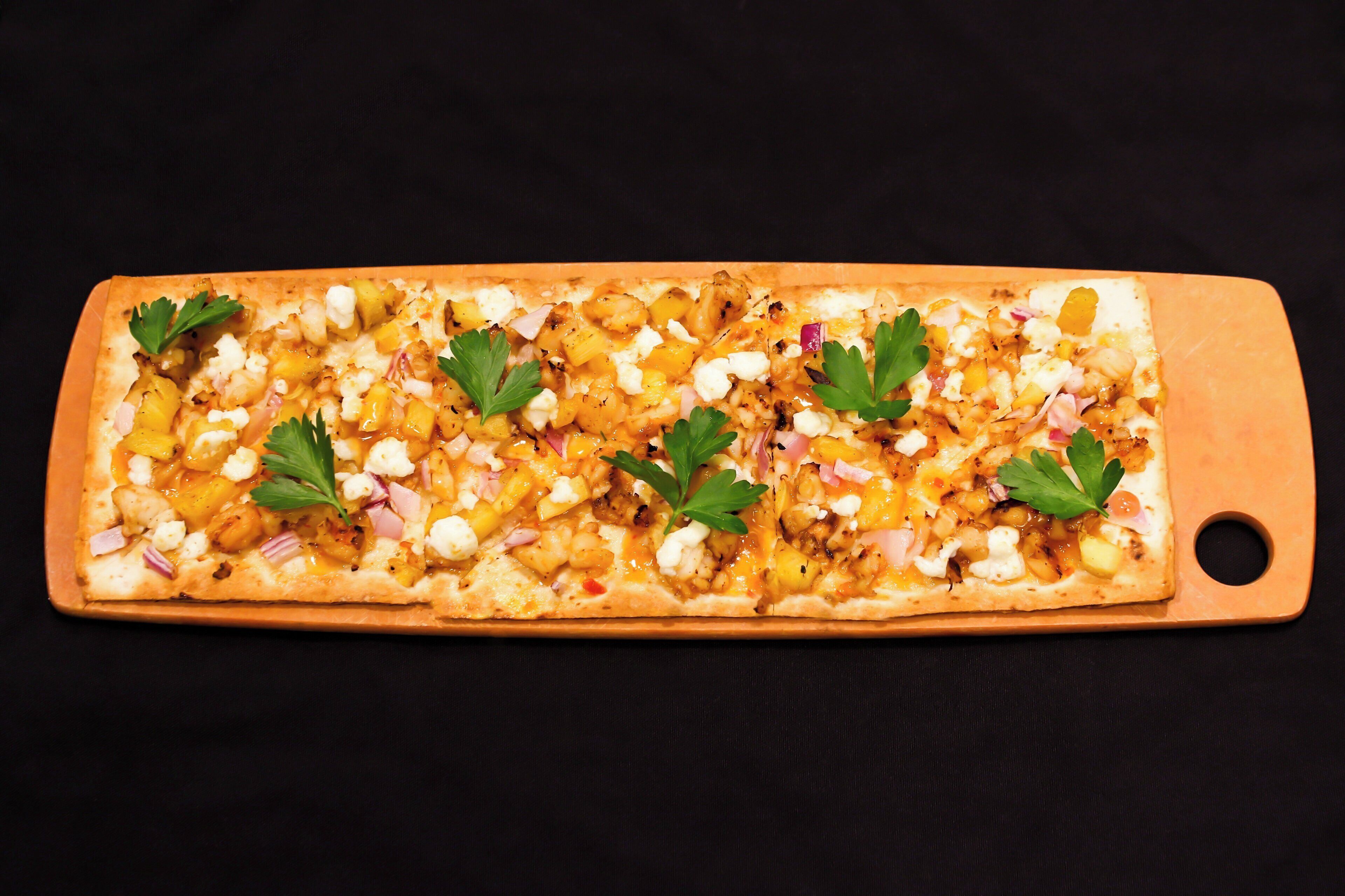 A rectangular pizza with various toppings and garnished with parsley, served on a wooden board.