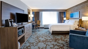 A hotel room with a bed, a desk with a television, a coffee maker, a chair, and a large window with curtains. - Holiday Inn Mississauga Toronto West by IHG (Mississauga)