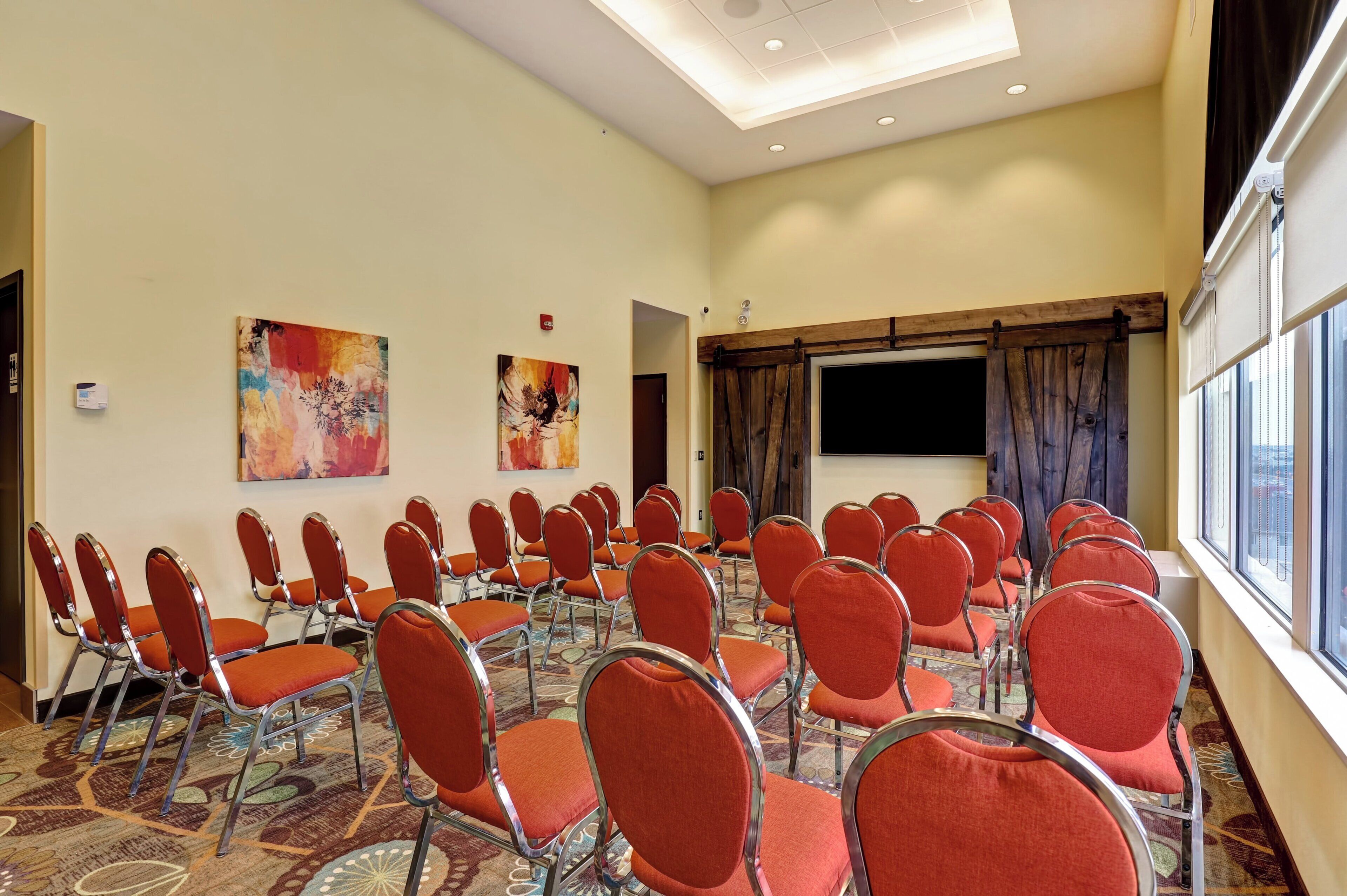 A conference room with rows of red chairs, a projector screen, and two abstract paintings on the walls.