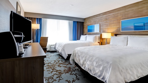 A hotel room with two beds, a desk with a TV, a lamp, and a large window with curtains. - Holiday Inn Mississauga Toronto West by IHG (Mississauga)