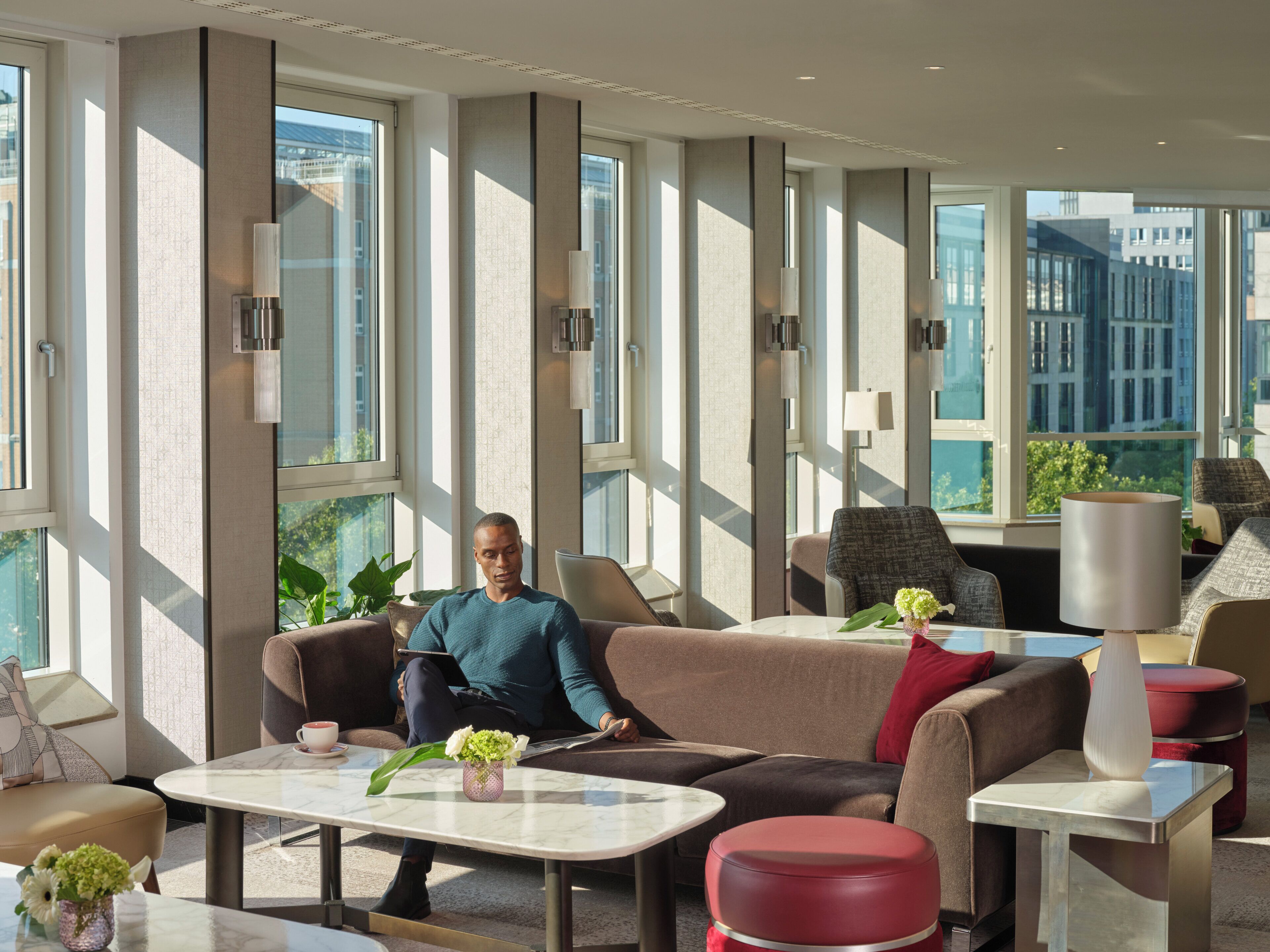 Un hall d’hôtel moderne doté de grandes fenêtres, d’un espace salon avec des canapés et une table basse, et offrant une vue sur le paysage urbain.