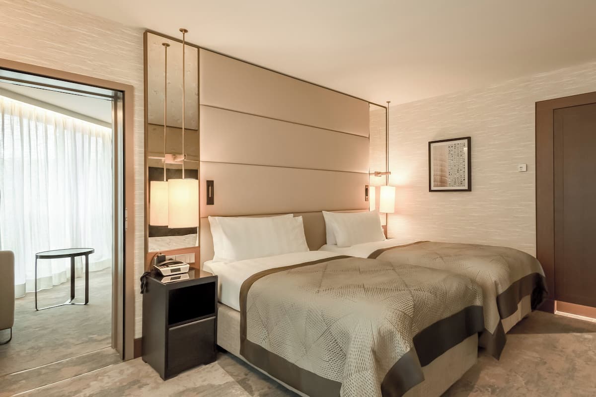 Moderni hotellihuone, jossa on suuri sänky, yöpöydät, peili ja ovi.