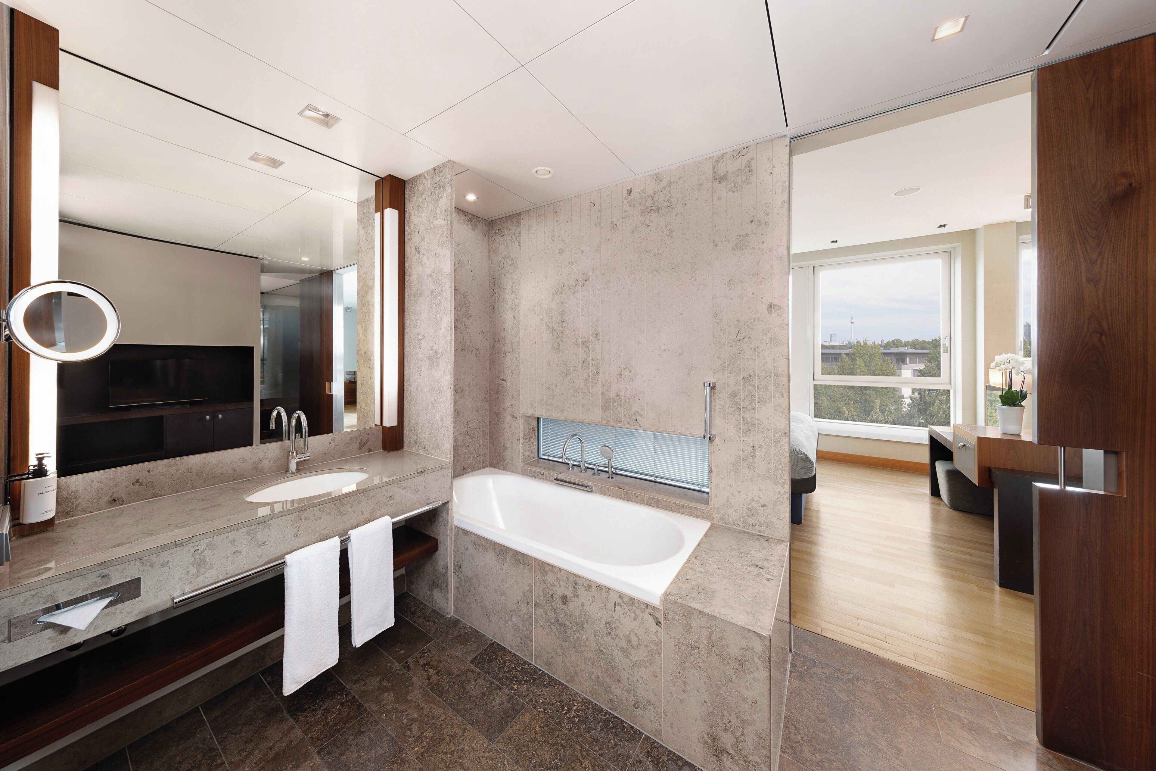 A modern bathroom with a large mirror, two sinks, a bathtub, and a large window offering a view.