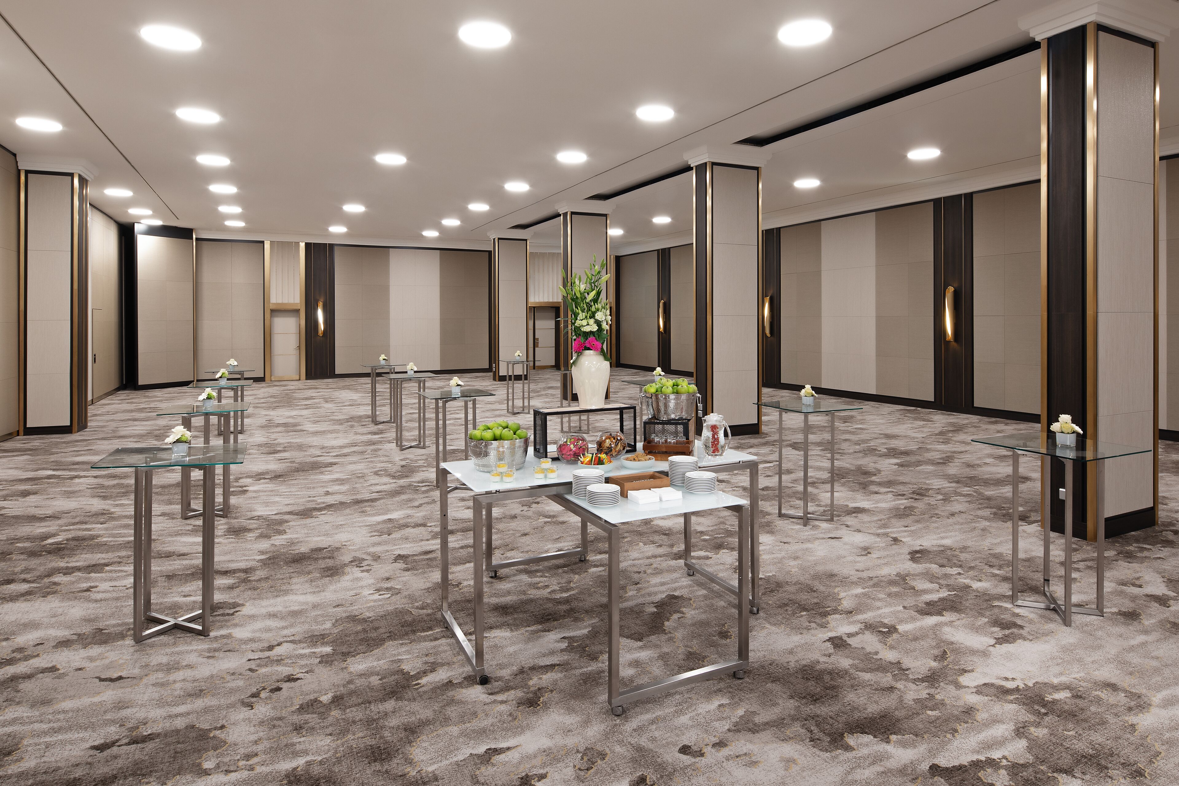 A spacious conference room with multiple tables, a large vase with flowers, and a carpeted floor.