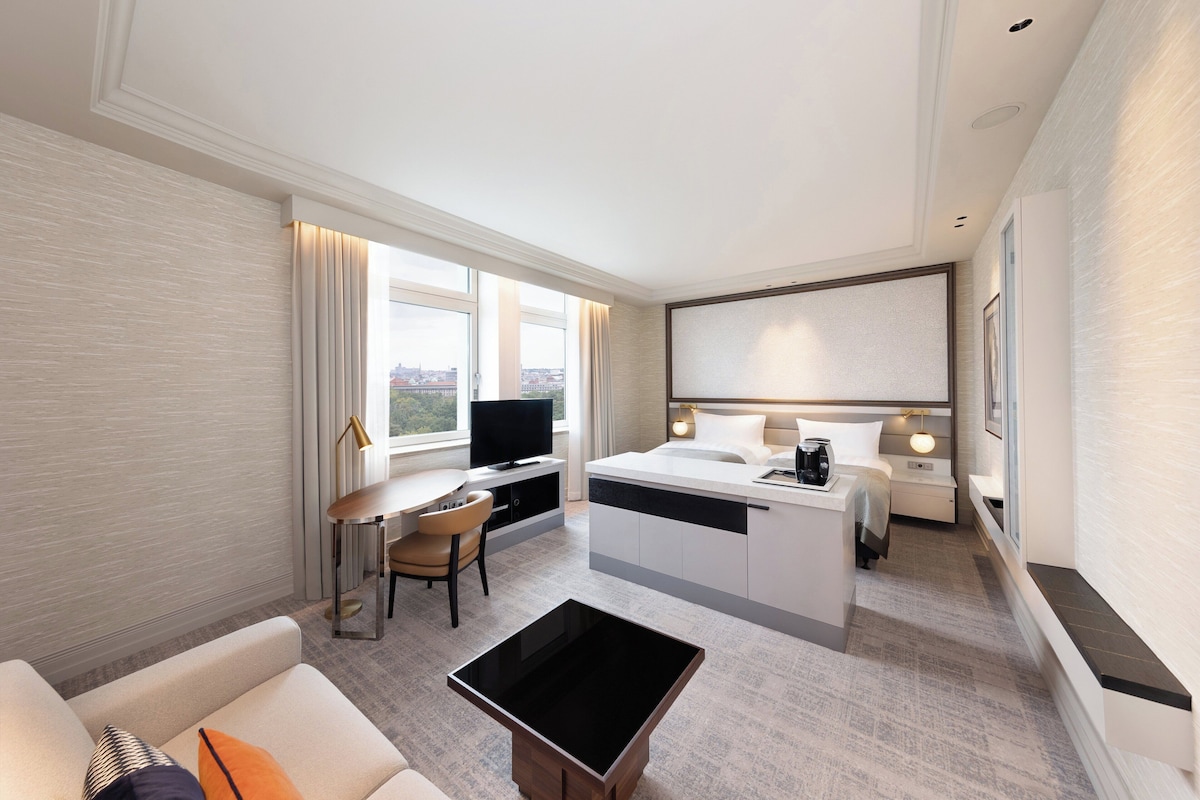 Habitación de hotel moderna con escritorio, cama, televisión y vistas de la ciudad.