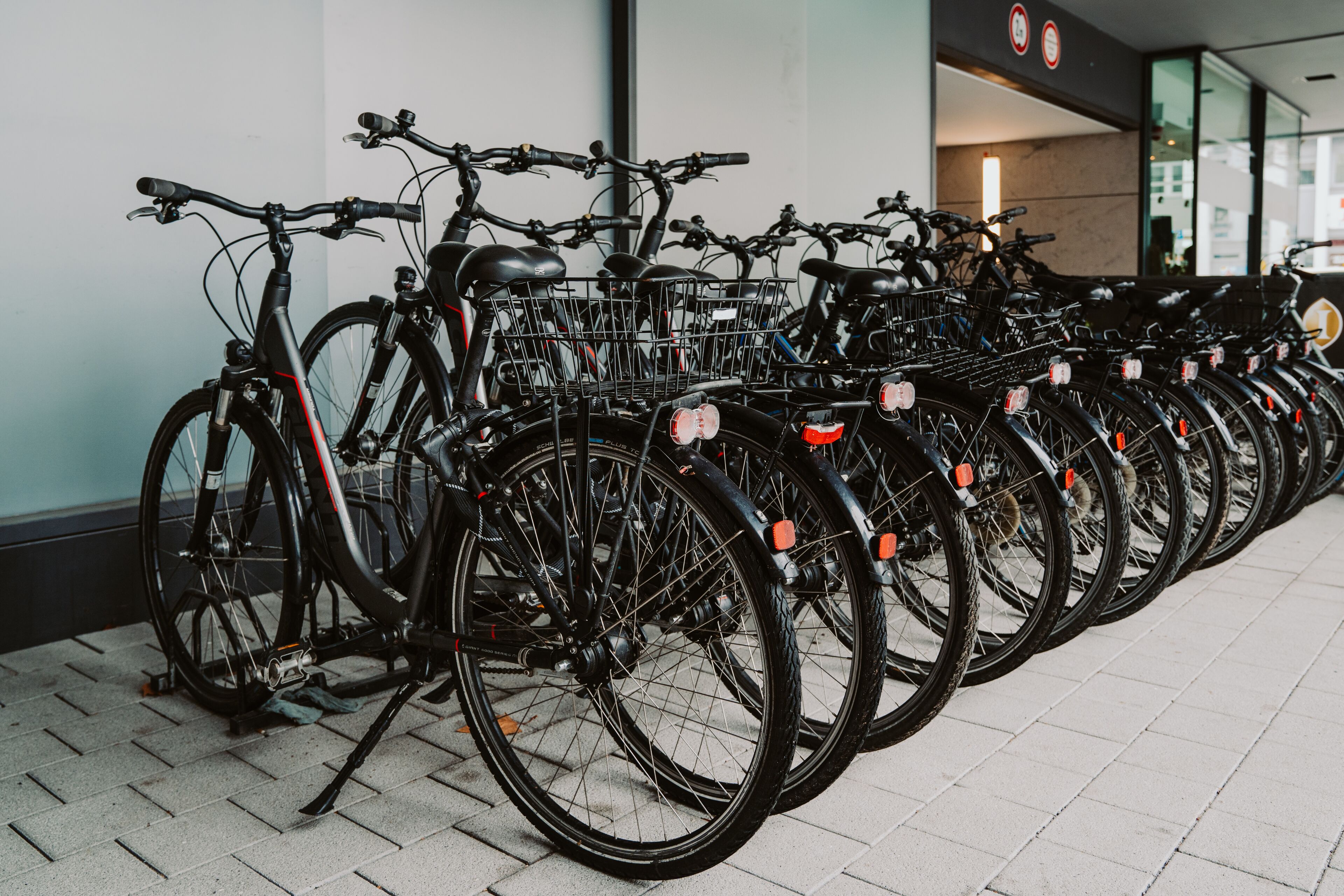 A row of bicycles parked in an indoor area with tiled flooring and a wall with a sign.