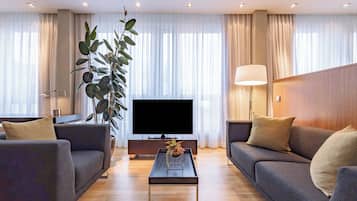 A modern living room with a flat-screen TV, two sofas, a coffee table, and a large plant.