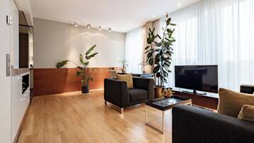 Een moderne woonkamer met een bank, een salontafel en een televisie. Er staan potplanten en een houten accentmuur.