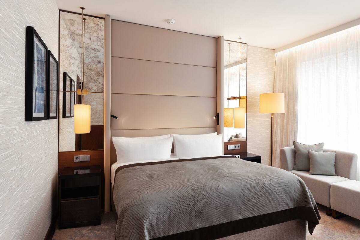 Moderni hotellihuone, jossa on suuri sänky, sohva ja yöpöytä, jossa on lamppu.