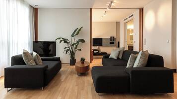 A modern living room with two black sofas, a wooden coffee table, and a large potted plant.