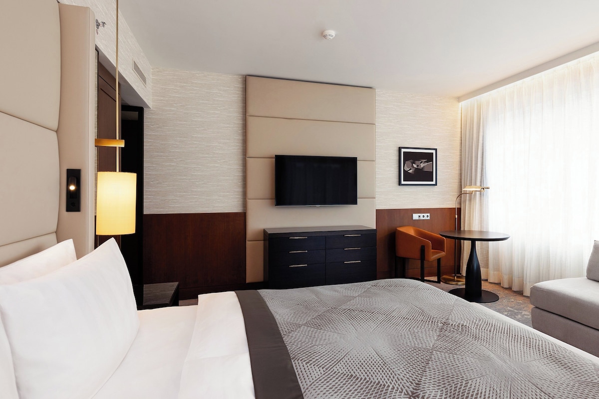 Una habitación de hotel con cama, televisión, escritorio, silla y sofá.