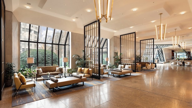 Un lobby espacioso con amplias ventanas, muebles modernos y una escalera central.