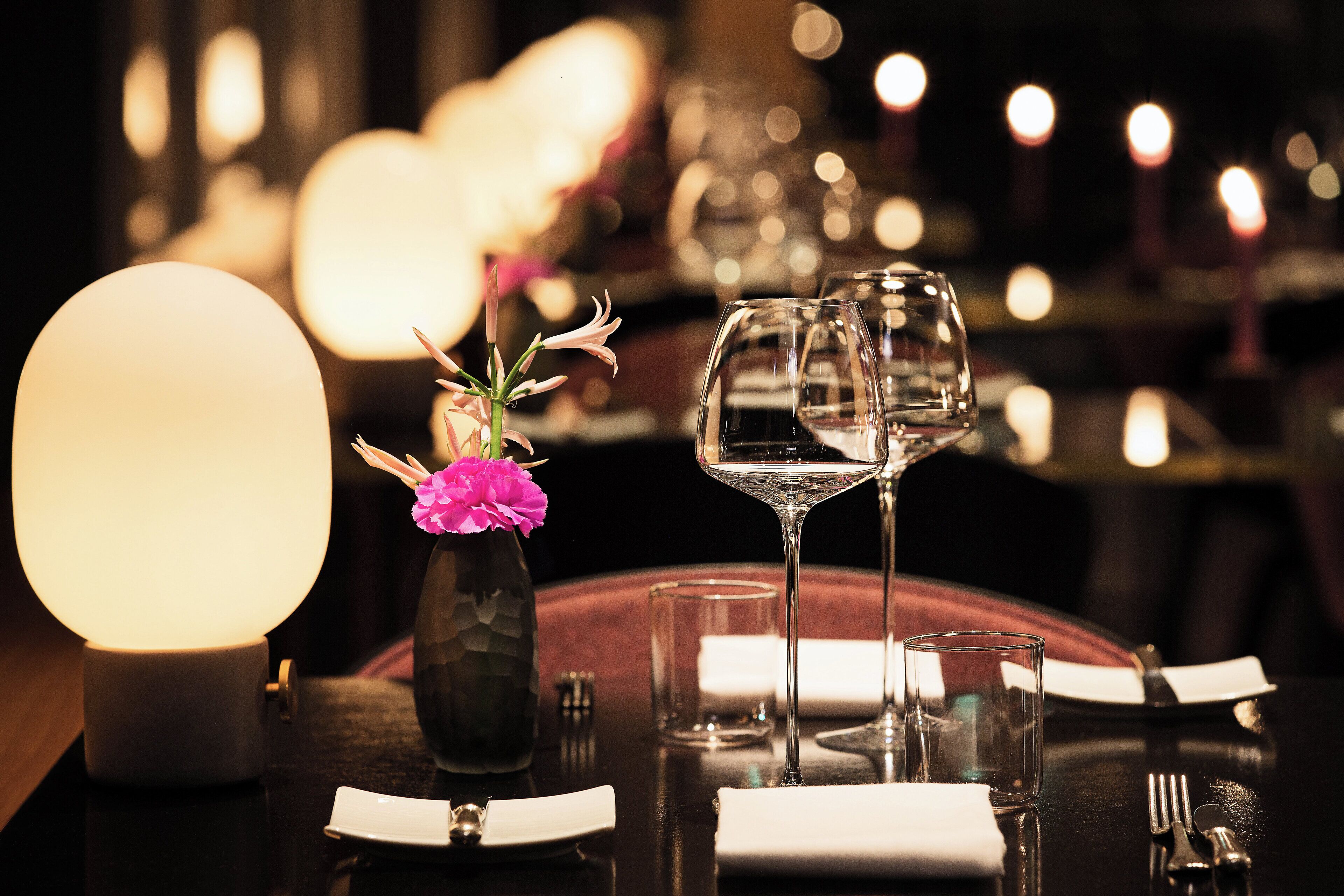 A dining table set with a candle, a vase with flowers, and wine glasses.
