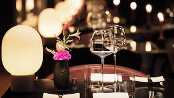 A dining table set with a candle, a vase with flowers, and wine glasses.