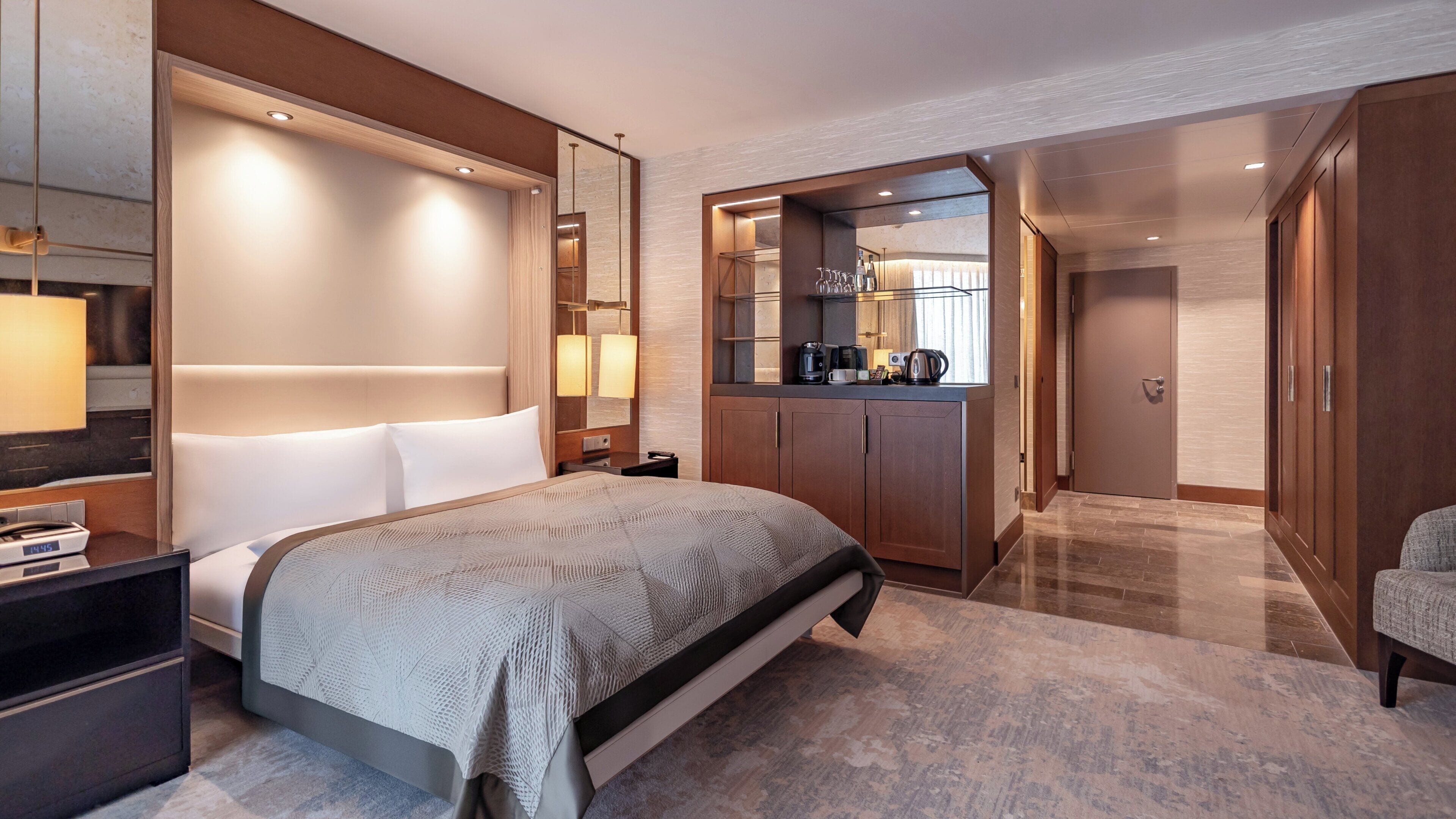 Habitación de hotel con una cama grande, un escritorio con lámpara, minibar, espejo de baño y armario.