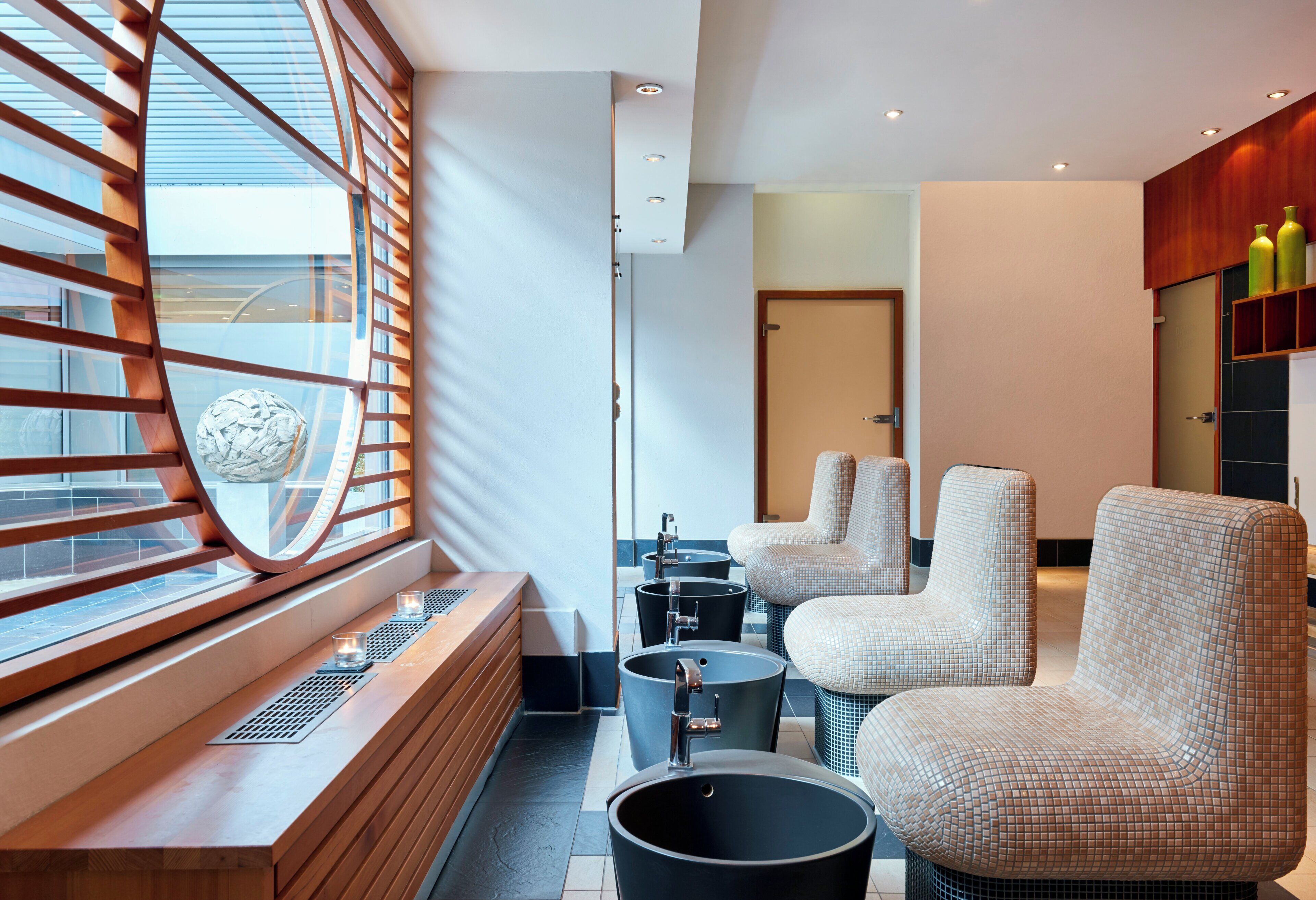 A modern bathroom with a large window, a bathtub, two sinks, and a seating area with chairs.