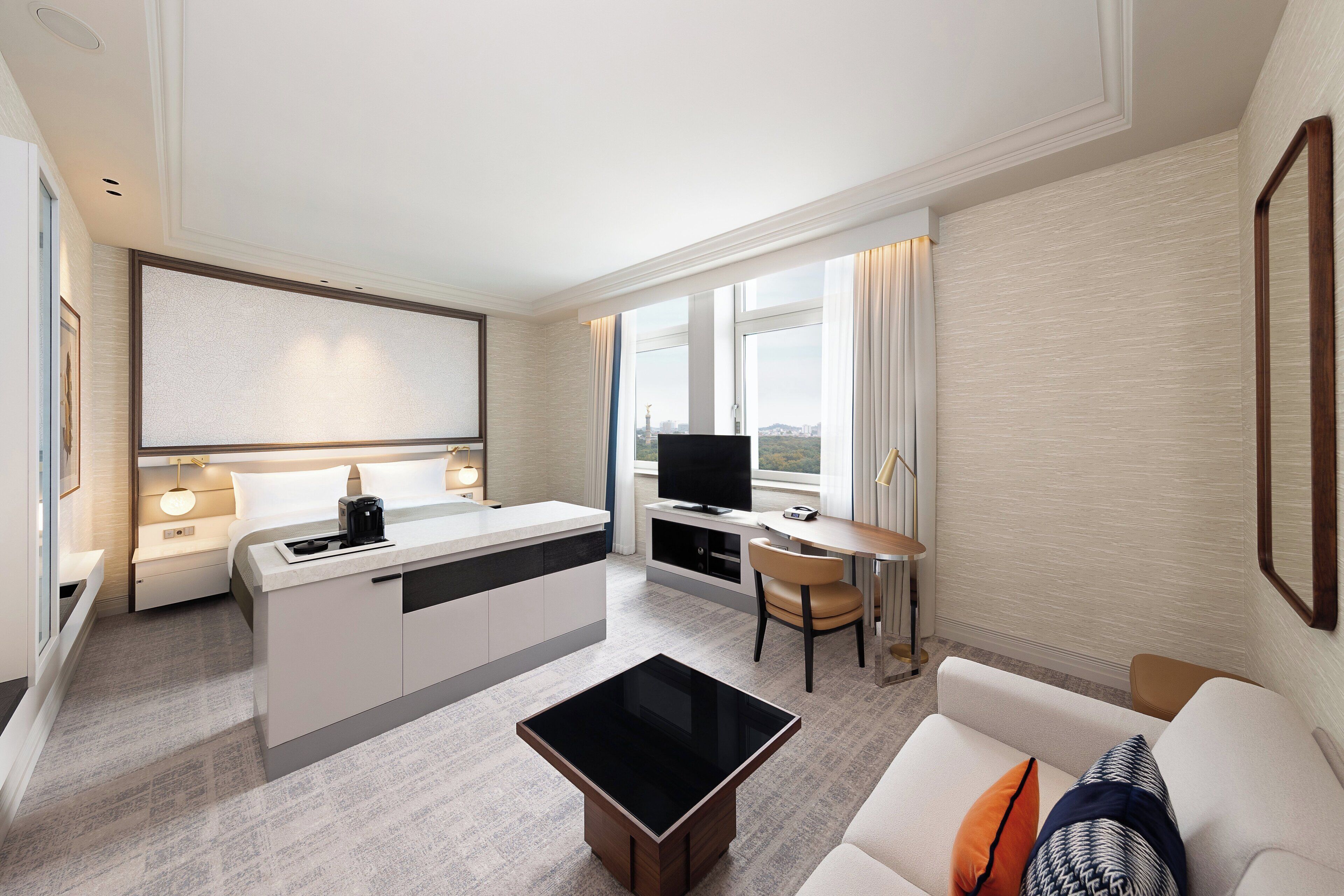 Moderni hotellihuone, jossa on pieni keittiö, ruokailutila, televisio ja sohva.