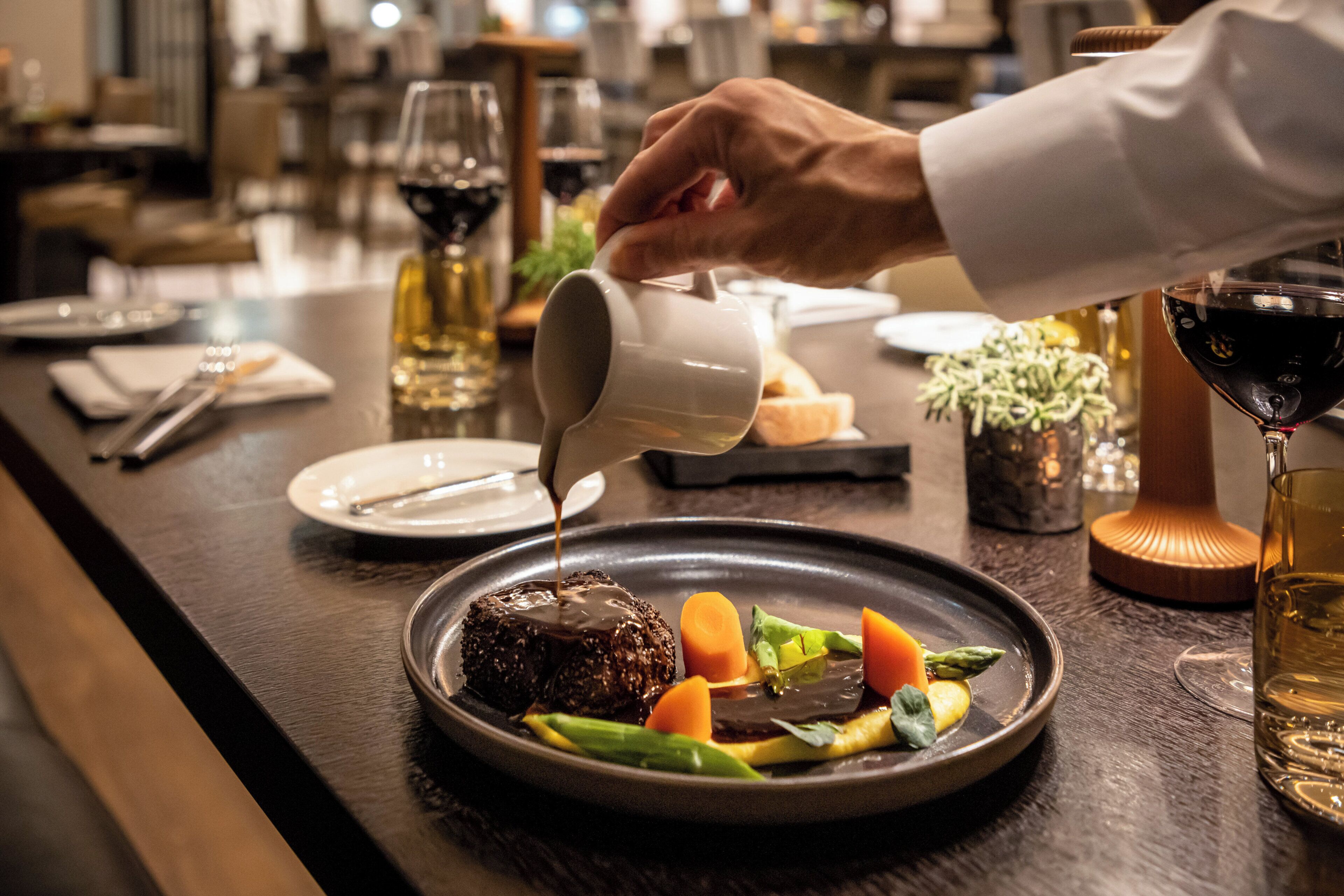 A person pouring a sauce over a plated dish with vegetables and meat.