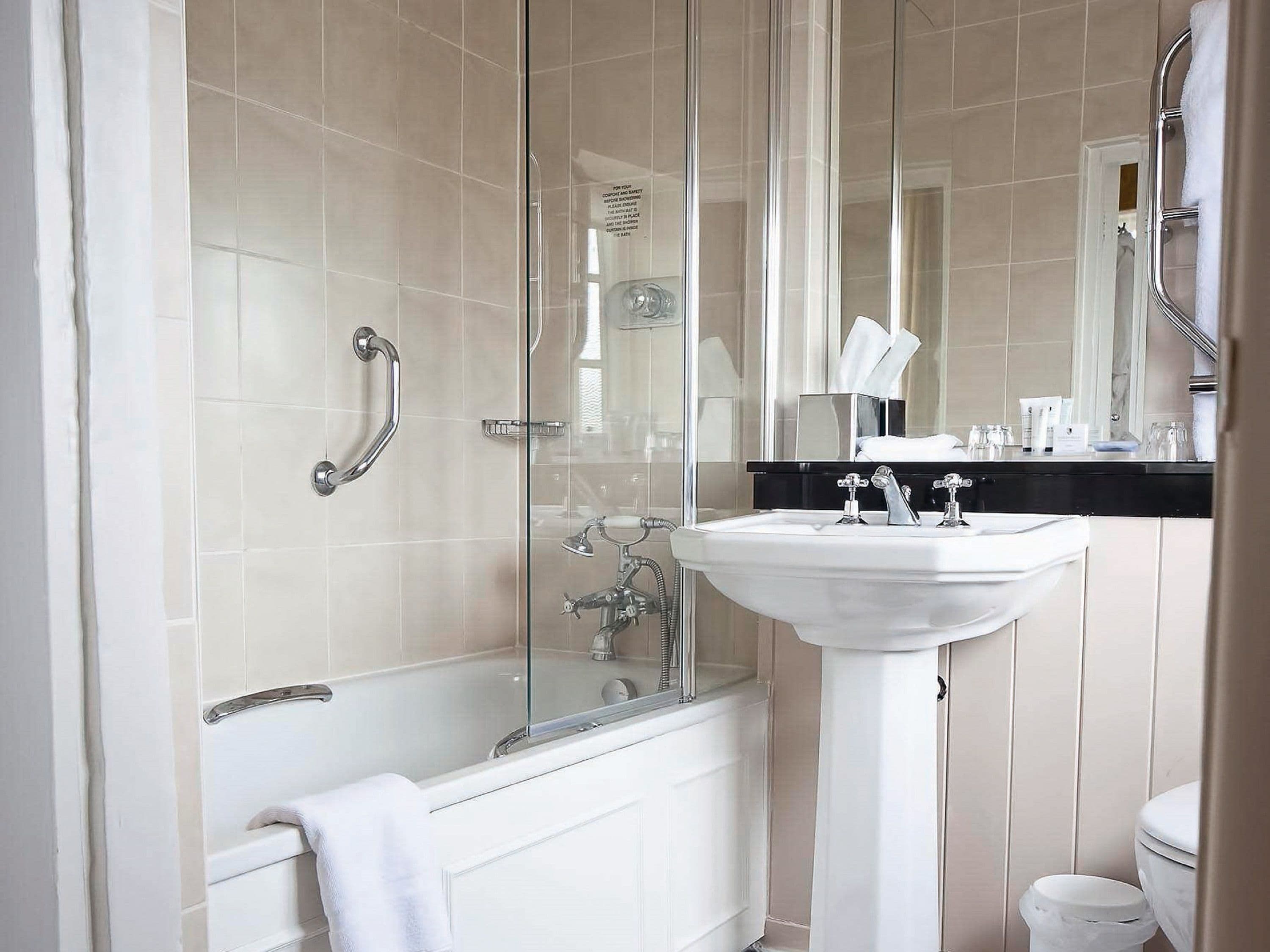 A modern bathroom with a glass-enclosed shower, a white bathtub, and a pedestal sink.