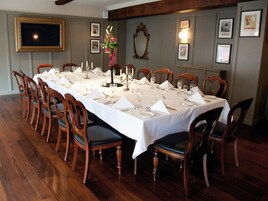 A formal dining room with a long table set for a meal, wooden chairs, and framed pictures on the walls.