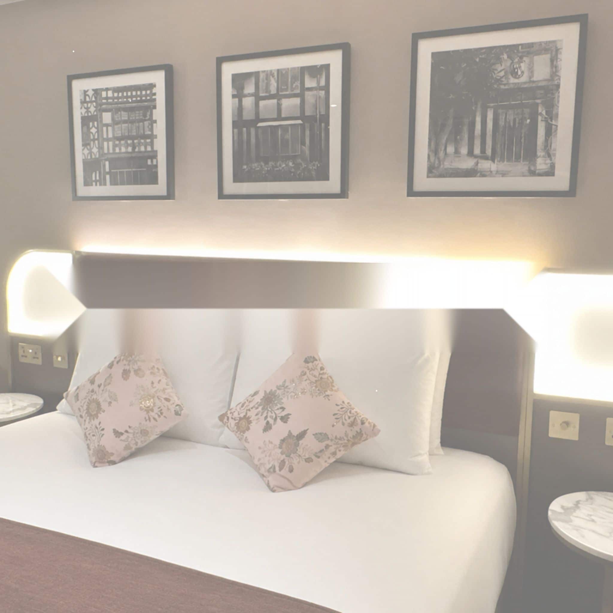 A hotel room with a bed, two bedside tables, and three framed pictures on the wall.