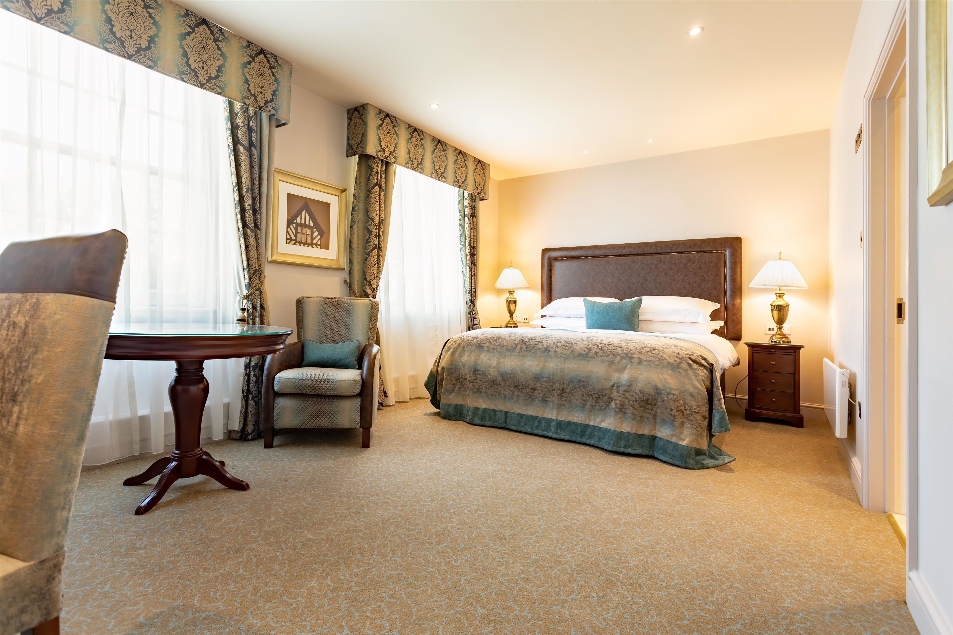 A hotel room with a large bed, a desk, a chair, and a nightstand with lamps.