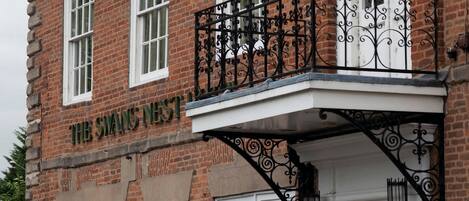 Un bâtiment en briques doté d’un balcon orné de balustrades en fer forgé et d’une enseigne indiquant : « The Swans Nest Inn ».