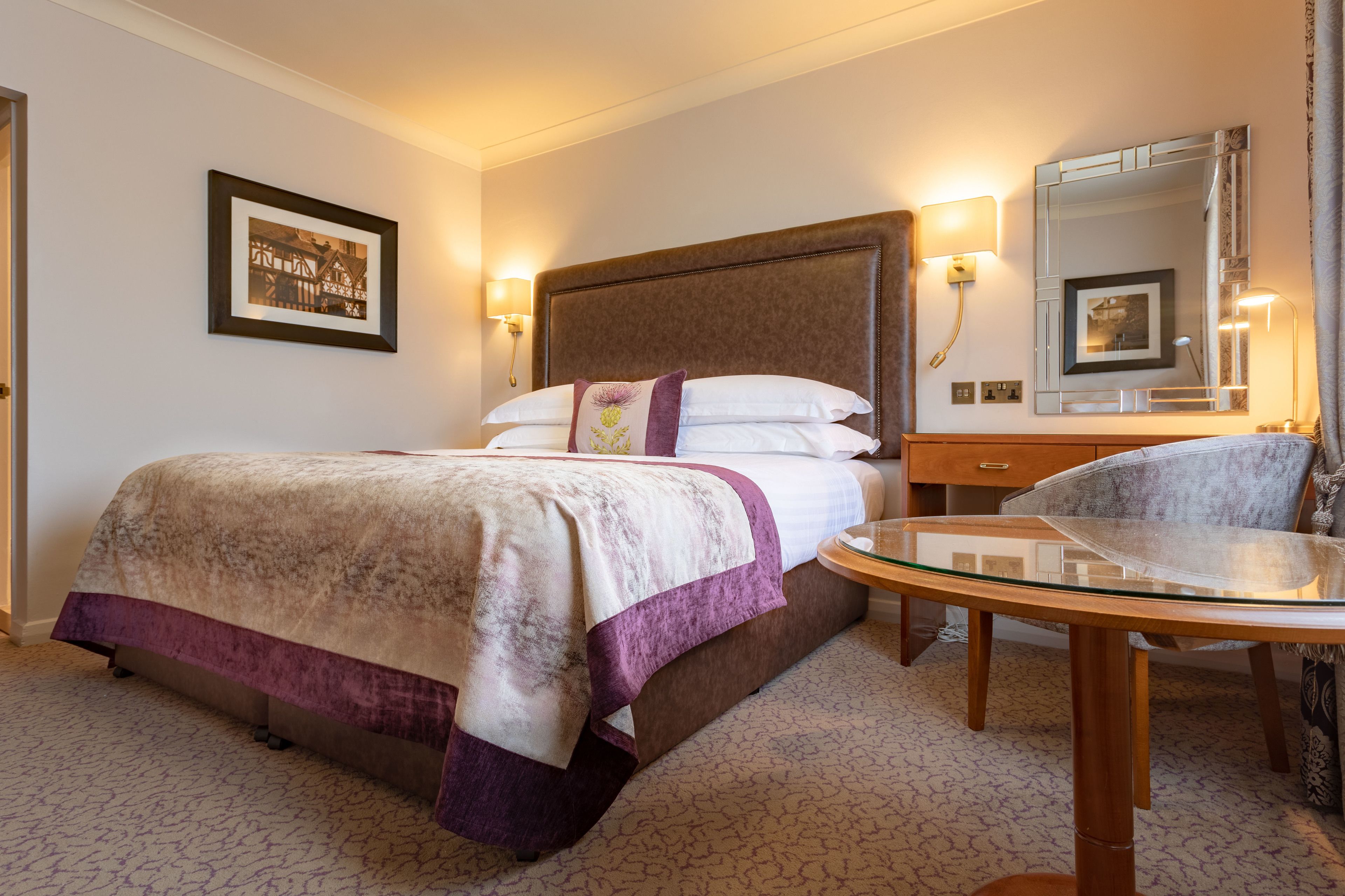 Quarto de hotel com cama, mesa de cabeceira, cadeira e um espelho grande.