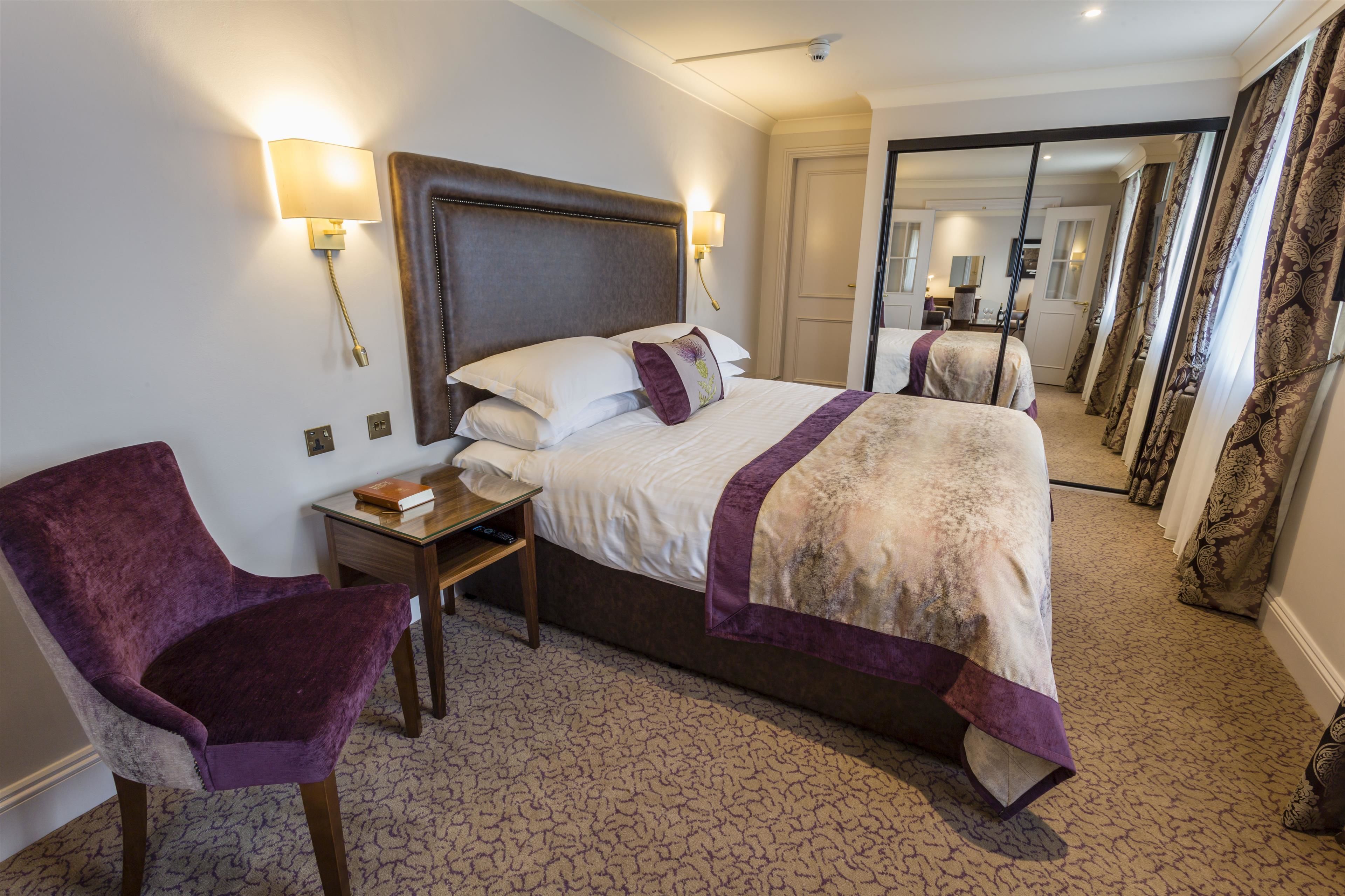 Una habitación de hotel con una cama grande, una silla, una mesita de noche y un espejo.