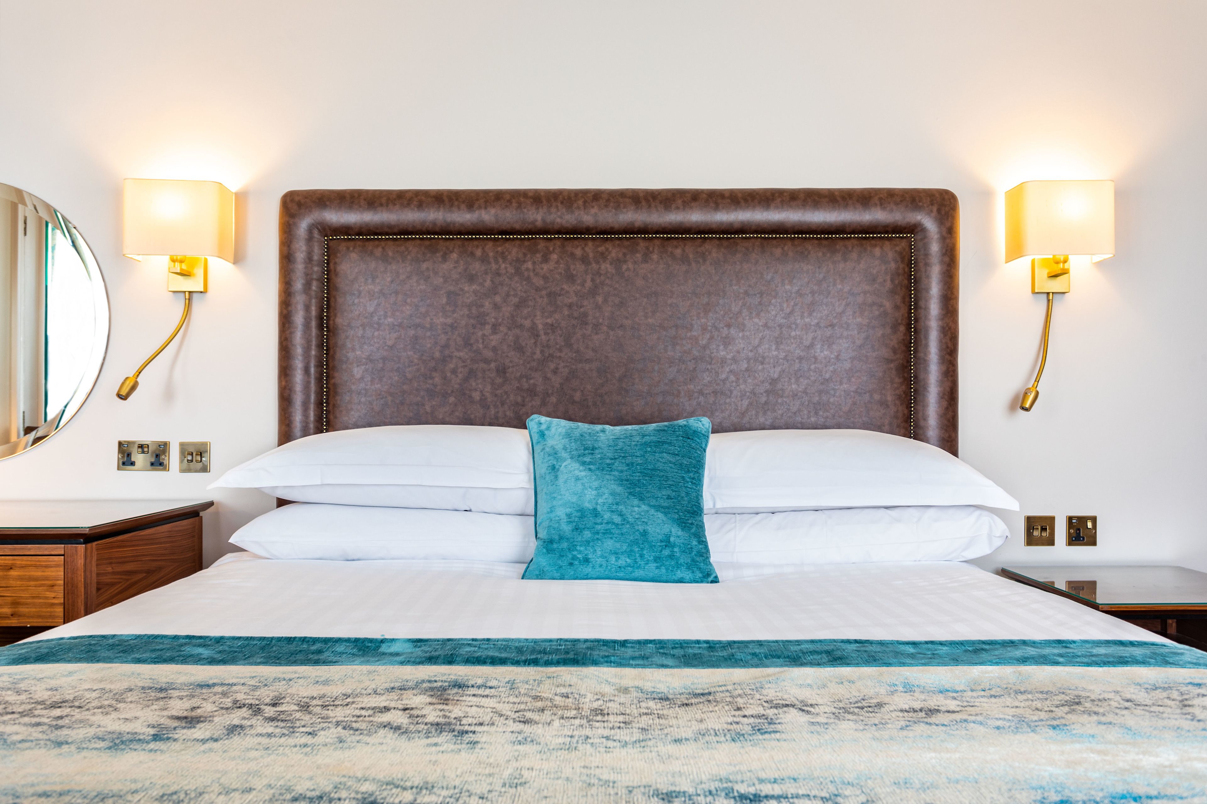 A hotel room with a large bed, two bedside lamps, a nightstand, and a mirror.