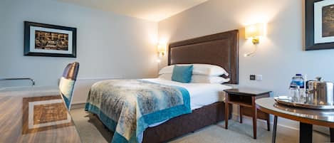 A hotel room with a bed, bedside table, chair, and a framed picture on the wall.