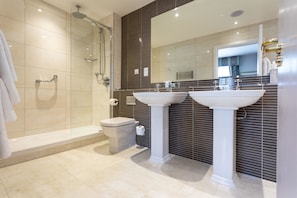 Enjoy a refreshing shower in the walk-in shower with a glass door, accompanied by a toilet and two pedestal sinks.