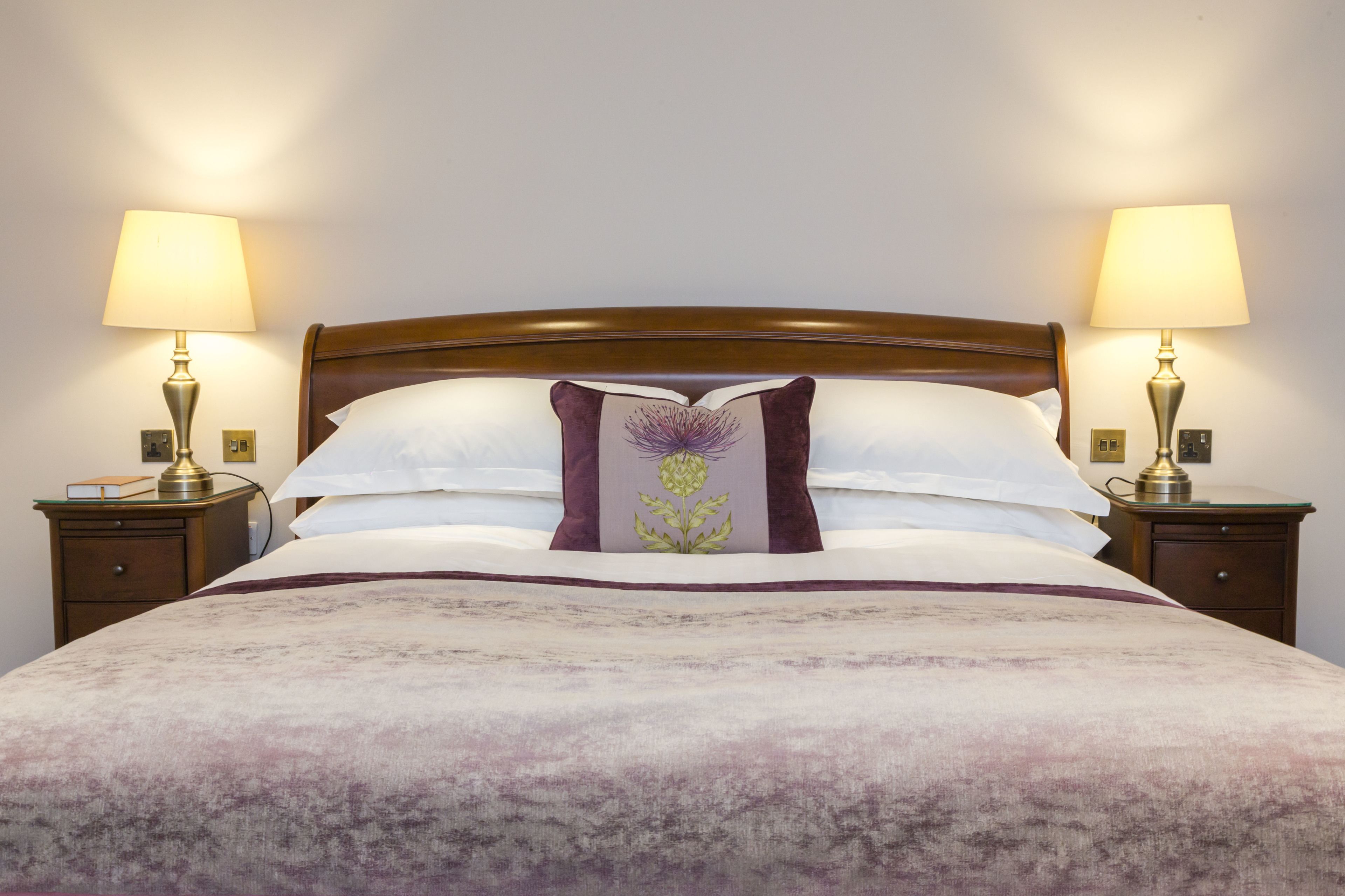A neatly made bed with a wooden headboard, two bedside lamps, and a decorative pillow.
