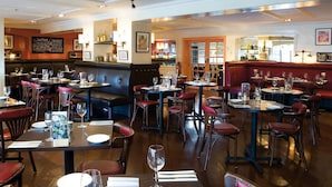 L’intérieur d’un restaurant présente plusieurs espaces de restauration, notamment des banquettes et des tables, et un bar visible à travers une porte ouverte.