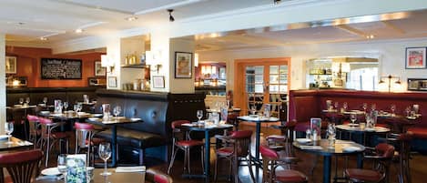 A restaurant interior with multiple seating areas, including booths and tables, and a bar visible through an open doorway.