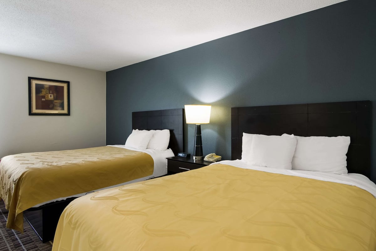A hotel room with two beds, each with a yellow bedspread, a bedside table with a lamp, and a framed picture on the wall.
